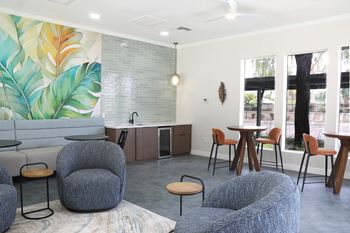 A room with a mural of leaves on the wall and grey chairs and tables.